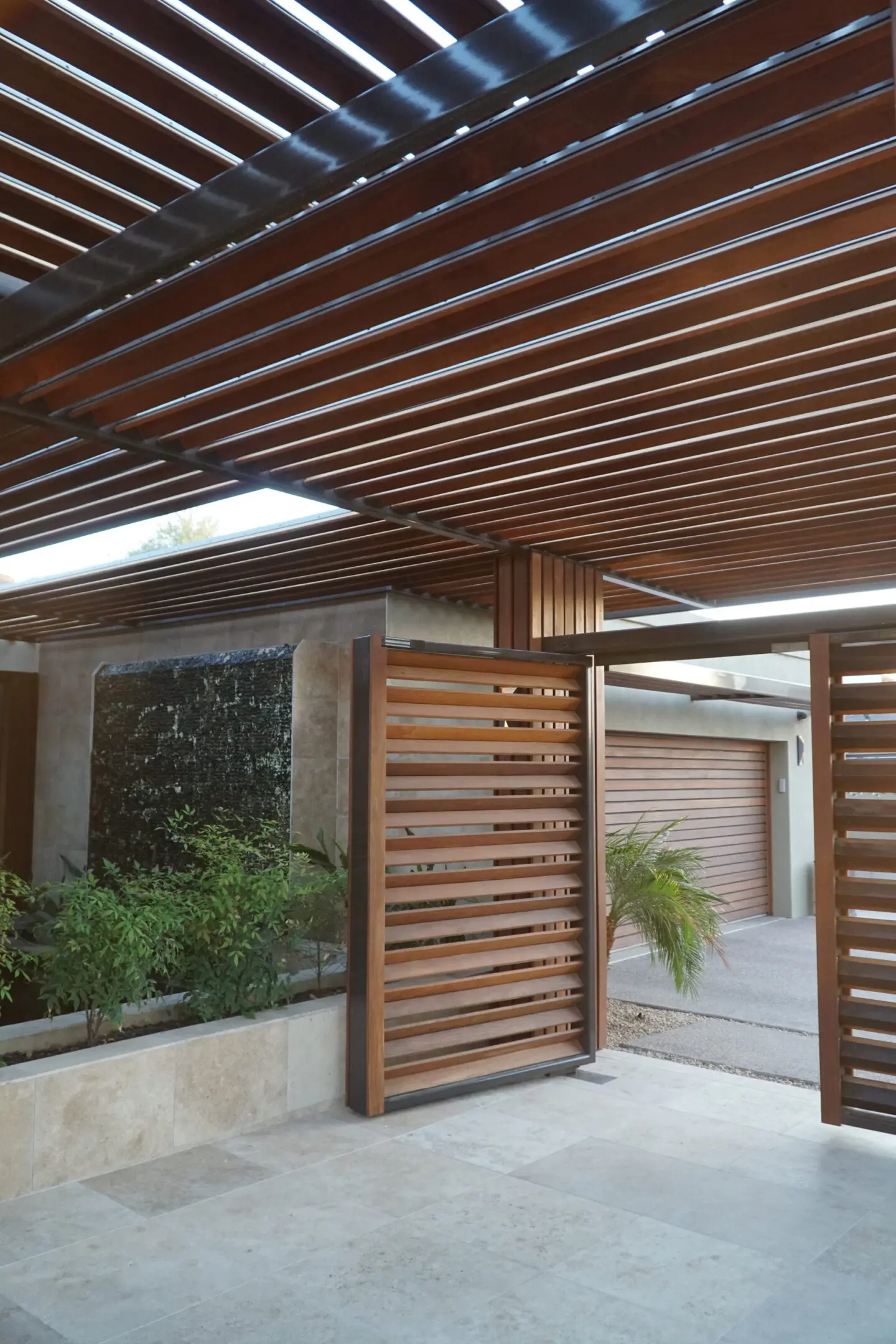 Modern wooden ceiling and gate with stone wall and plants.