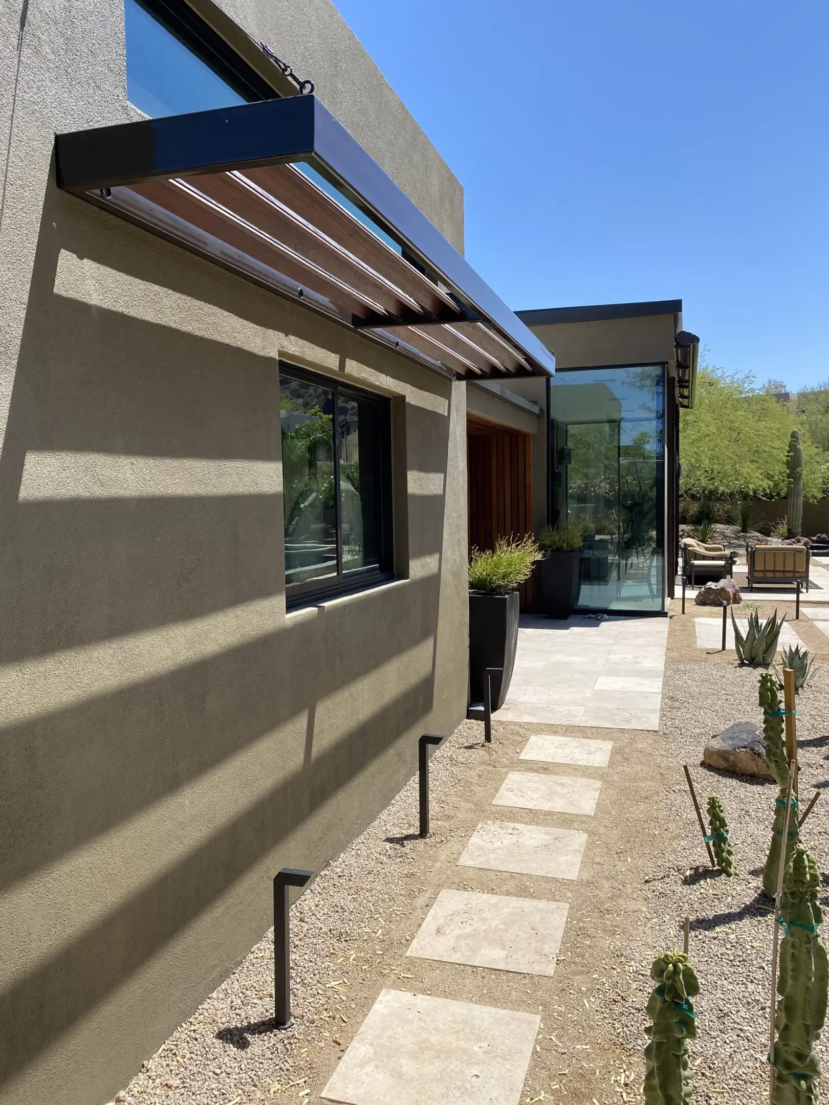 Modern patio with glass doors and desert landscaping under a pergola.