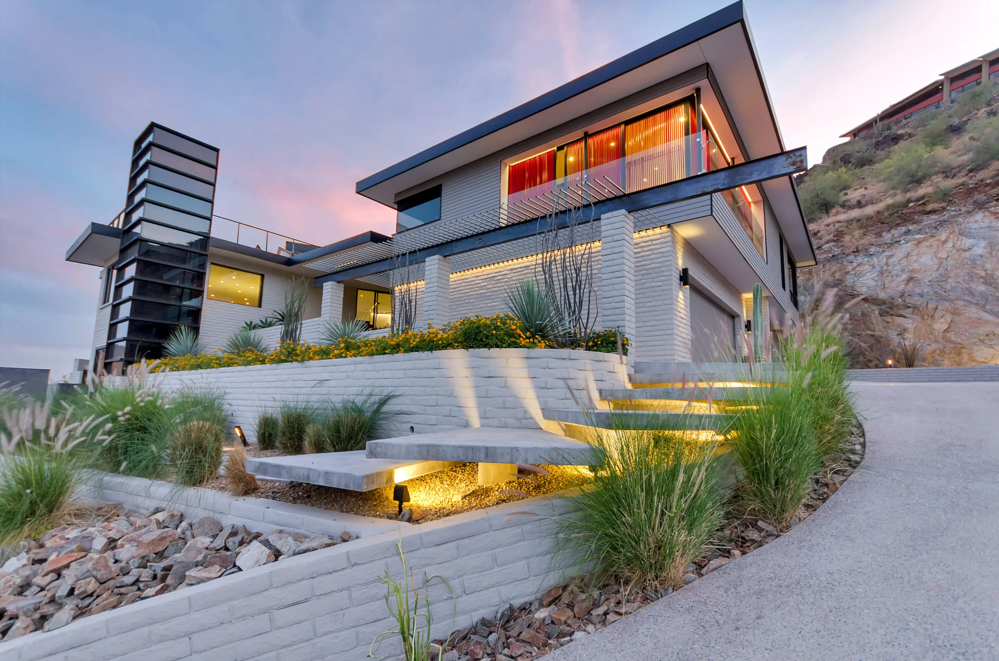 Modern house exterior at sunset with landscaped garden and ambient lighting.