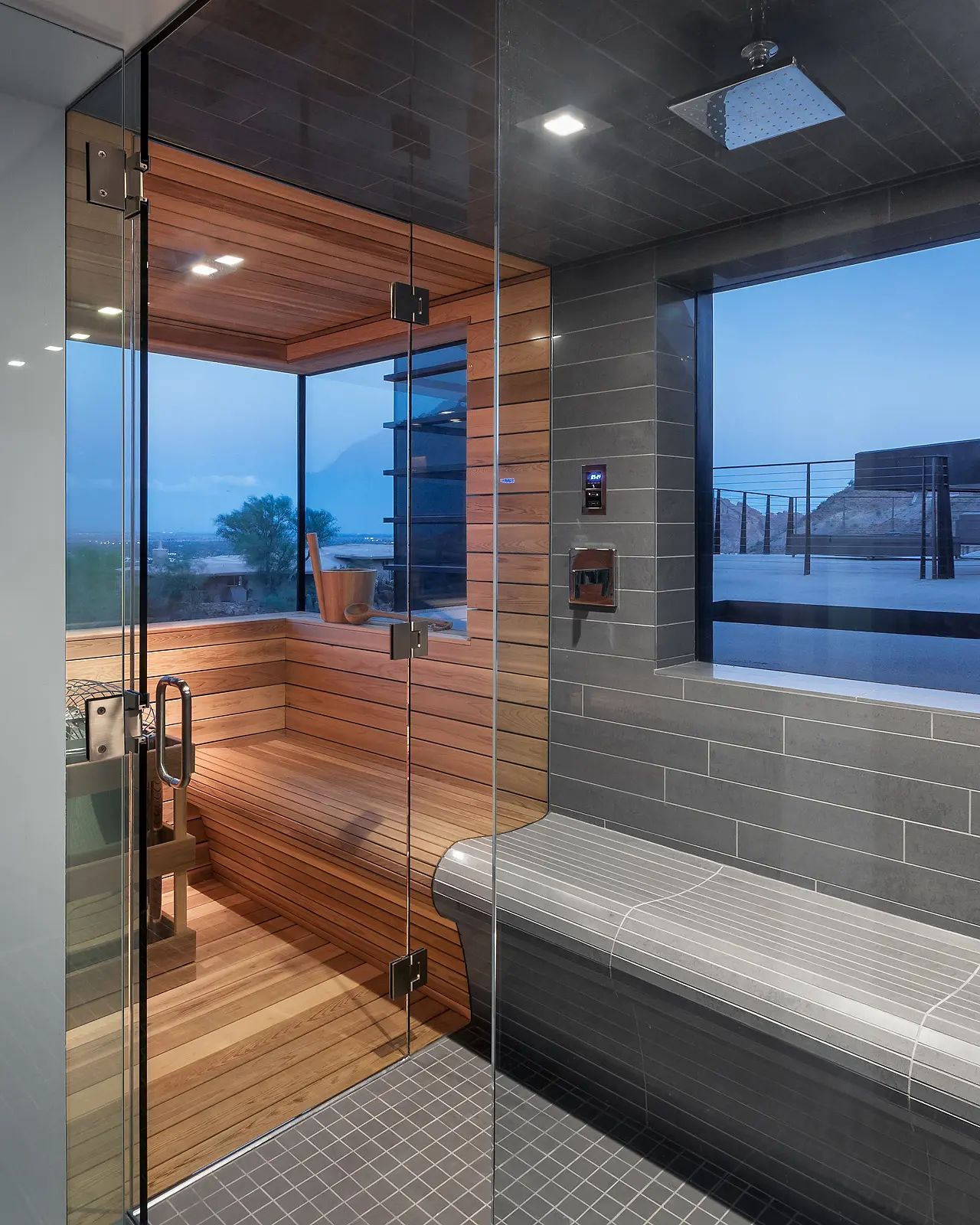 Modern sauna with glass walls overlooking a scenic view at dusk.