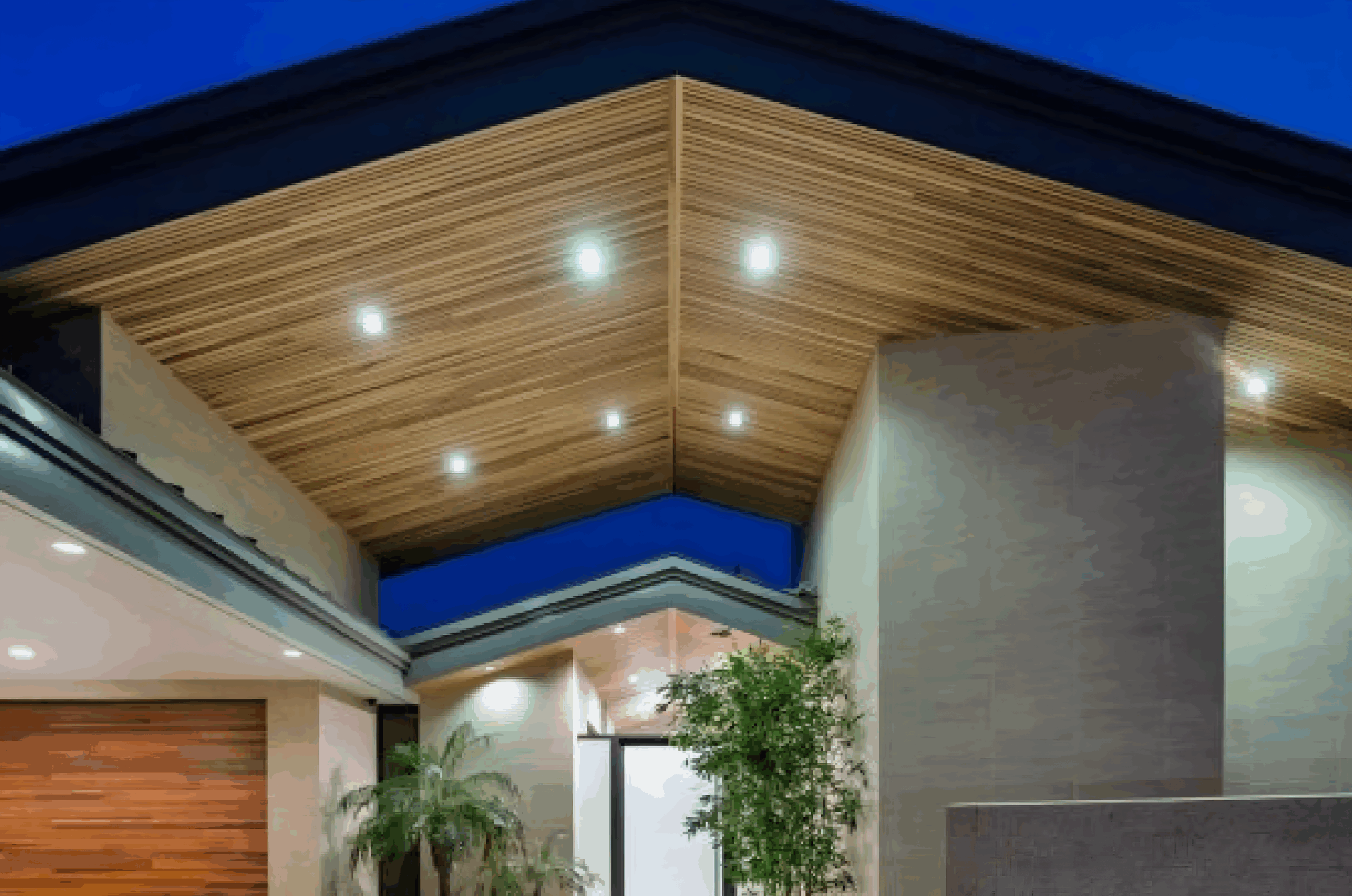 Modern house entrance with wooden ceiling and recessed lighting at dusk.